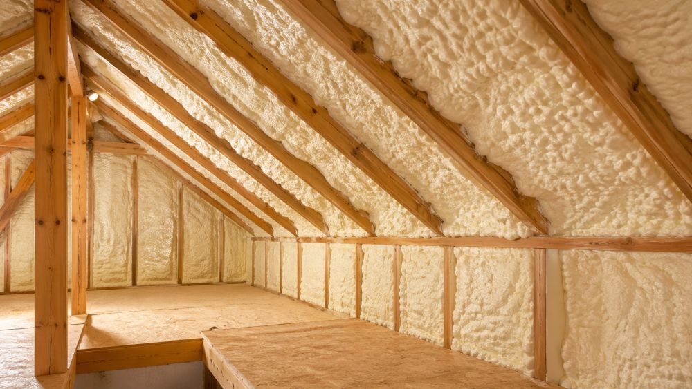 Spray foam insulation installed in an attic in Burbank, CA by Pure Eco shows thick expanding foam sealing gaps between wooden rafters and roof decking. The insulation covers all exposed surfaces and helps reduce air leaks, improve indoor comfort, and lower energy bills. Pure Eco provides attic insulation services across Burbank with clean installation and code-compliant methods. For service details or a free inspection, call Pure Eco at (877) 870-7998.