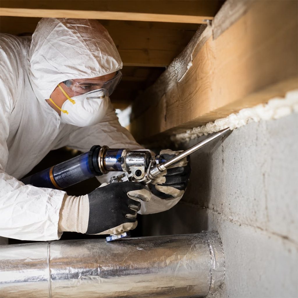 Professional air sealing technician applying foam sealant around gaps in a crawl space in Chatsworth, CA.