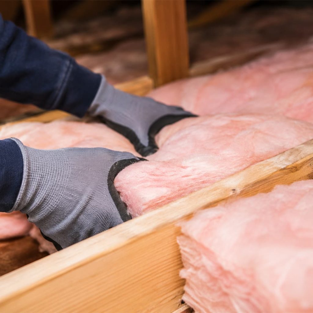 Close-up of a technician installing fiberglass attic insulation between wooden joists in Northridge, CA.