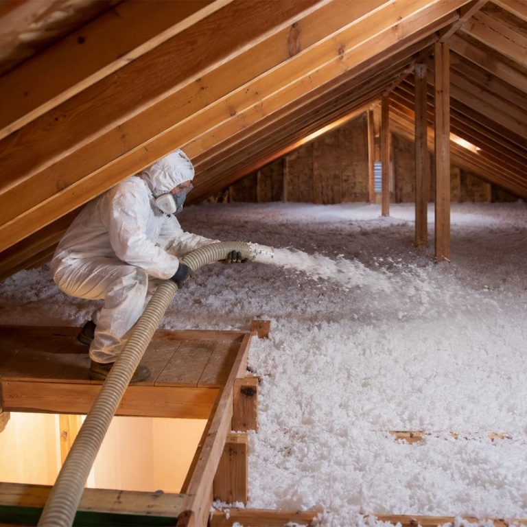 Technician installing blown-in insulation across an attic floor using a large insulation hose.