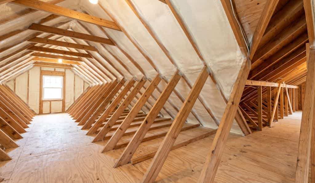 A newly insulated residential attic featuring clean, white spray foam completely sealing the roofline and rafters.