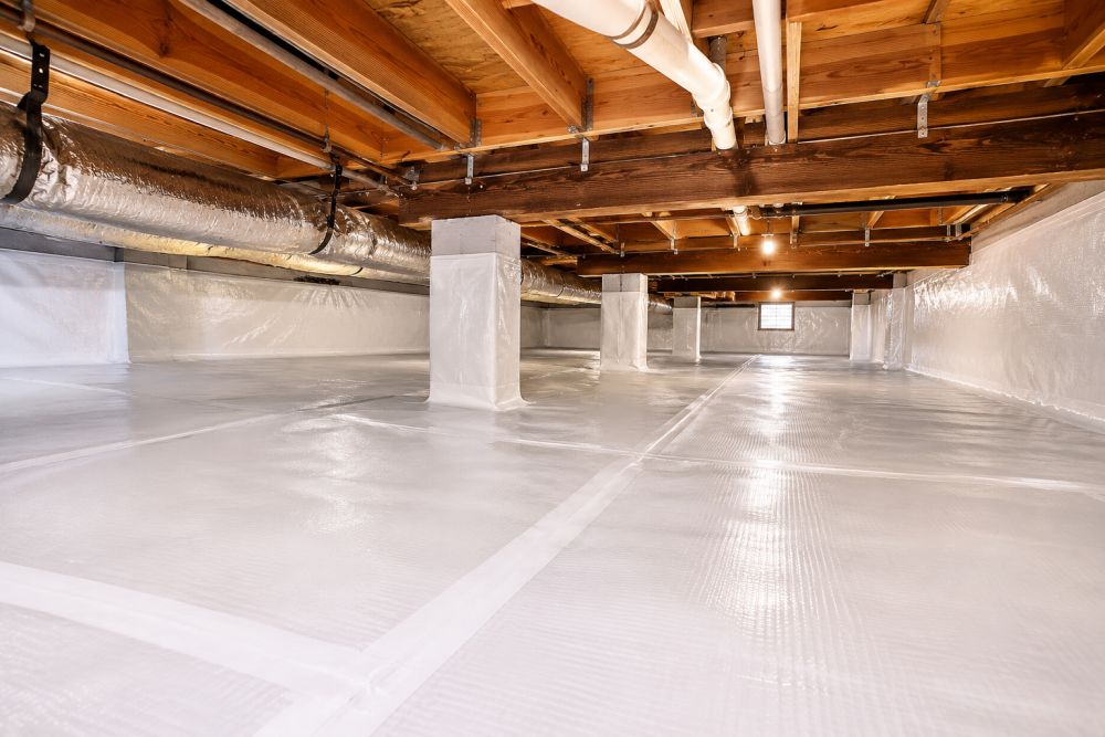 A residential crawl space in Woodland Hills, California featuring a professionally installed white vapor barrier system across the ground and foundation walls. The image shows sealed vapor barrier seams, exposed wooden floor joists, support piers, utility pipes, and structural framing above the encapsulated crawl space floor. Pure Eco provides vapor barrier installation services in Woodland Hills, CA to help reduce moisture intrusion and improve crawl space conditions.