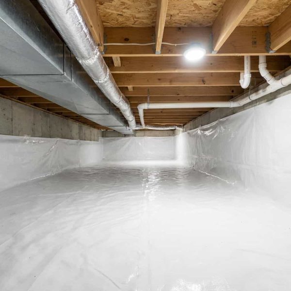 Clean crawl space with white vapor barrier and PVC pipes underneath wooden joists
